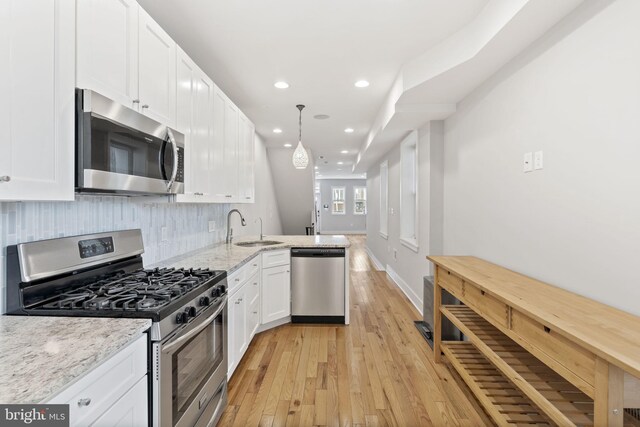 kitchen with white cabinets, light wood-style floors, stainless steel appliances, and a sink