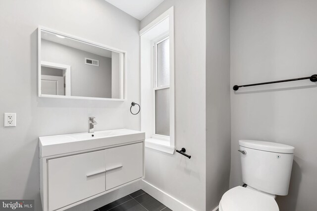half bath with tile patterned floors, visible vents, toilet, vanity, and baseboards