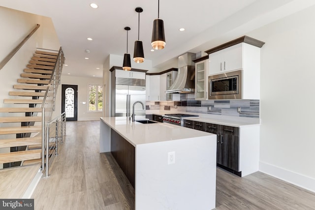 kitchen with recessed lighting, a sink, built in appliances, wall chimney range hood, and light countertops