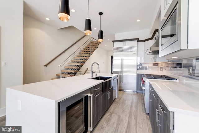 kitchen with a sink, wine cooler, high end appliances, light wood-type flooring, and light countertops