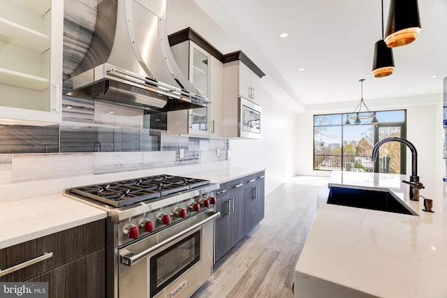 kitchen featuring range hood, a sink, light wood-style flooring, hanging light fixtures, and appliances with stainless steel finishes