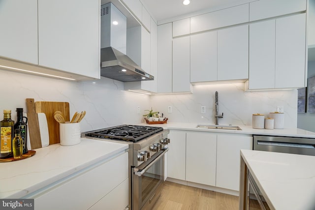 kitchen with wall chimney exhaust hood, a sink, white cabinetry, and appliances with stainless steel finishes