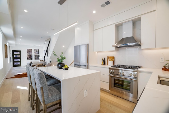 kitchen featuring visible vents, wall chimney exhaust hood, stainless steel appliances, and modern cabinets