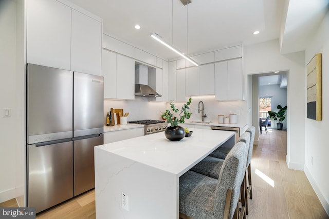 kitchen featuring recessed lighting, a sink, freestanding refrigerator, wall chimney exhaust hood, and a kitchen island