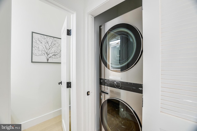 laundry area featuring stacked washer and dryer, wood finished floors, baseboards, and laundry area