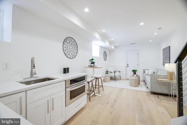 kitchen featuring recessed lighting, light wood-type flooring, oven, and a sink