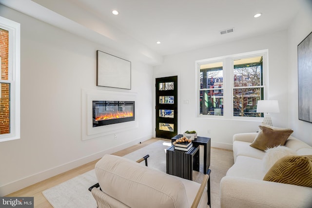 living area featuring a glass covered fireplace, baseboards, visible vents, and recessed lighting