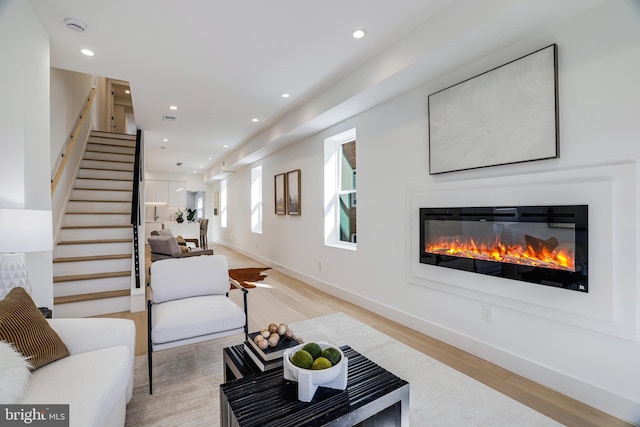 living area featuring light wood-type flooring, a glass covered fireplace, baseboards, and stairs