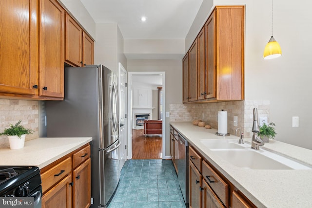 kitchen featuring appliances with stainless steel finishes, a sink, light countertops, brown cabinetry, and tasteful backsplash