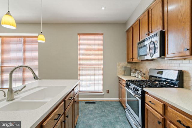 kitchen with appliances with stainless steel finishes, a sink, brown cabinetry, tasteful backsplash, and pendant lighting
