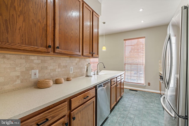 kitchen with brown cabinetry, a sink, appliances with stainless steel finishes, backsplash, and hanging light fixtures