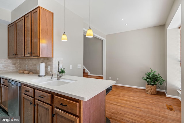 kitchen featuring tasteful backsplash, stainless steel dishwasher, a sink, light countertops, and light wood-style floors