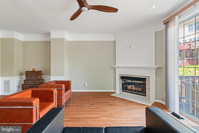 living area with a high end fireplace, a ceiling fan, wood finished floors, and ornamental molding