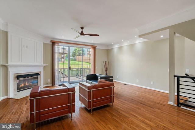 living room featuring a ceiling fan, a premium fireplace, hardwood / wood-style floors, and ornamental molding