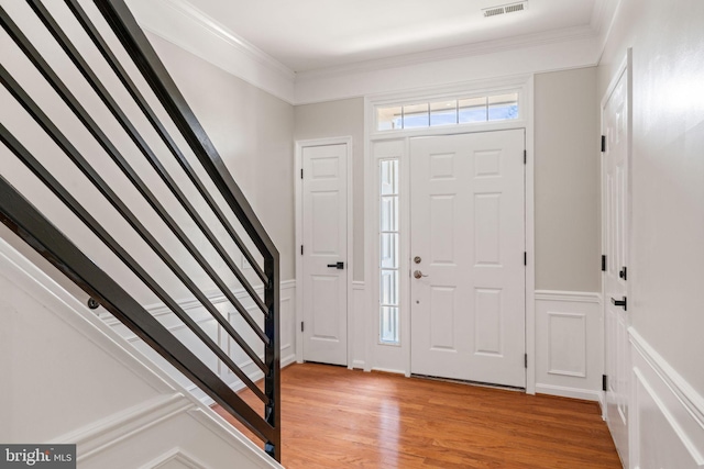 entryway featuring crown molding, wainscoting, light wood finished floors, stairs, and visible vents