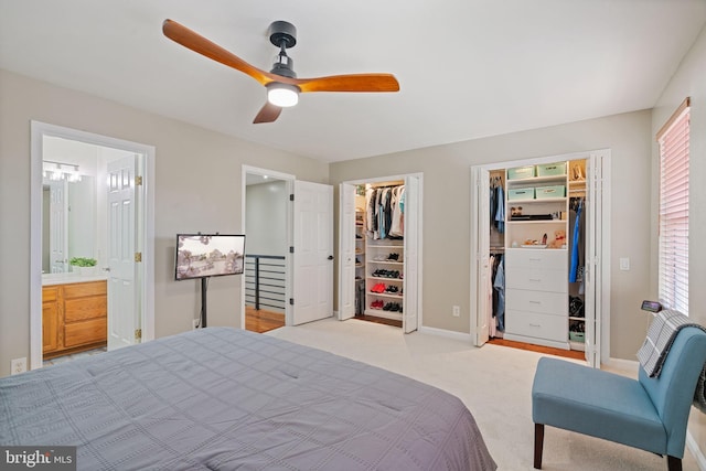 bedroom featuring baseboards, ensuite bathroom, light carpet, and ceiling fan