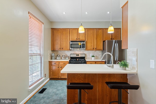 kitchen featuring brown cabinets, appliances with stainless steel finishes, light countertops, a peninsula, and decorative backsplash
