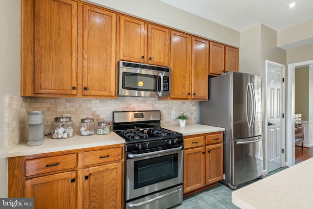 kitchen with light countertops, brown cabinetry, stainless steel appliances, decorative backsplash, and light tile patterned floors