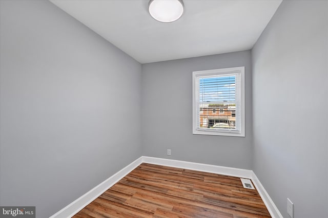 empty room featuring baseboards, wood finished floors, and visible vents