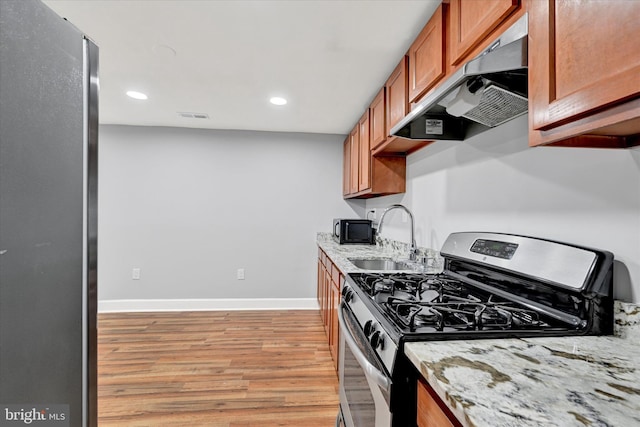 kitchen featuring a sink, light wood-style floors, stainless steel gas stove, brown cabinetry, and under cabinet range hood