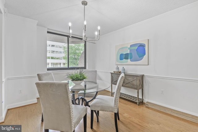 dining space with wood finished floors, a chandelier, ornamental molding, baseboards, and a textured ceiling