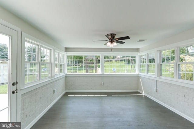 unfurnished sunroom featuring baseboards, visible vents, brick wall, and wood finished floors