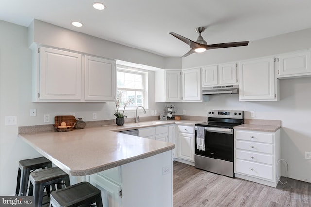 kitchen with stainless steel range with electric stovetop, a peninsula, a kitchen breakfast bar, white cabinetry, and under cabinet range hood