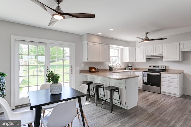 kitchen featuring stainless steel range with electric stovetop, a peninsula, ceiling fan, white cabinetry, and under cabinet range hood