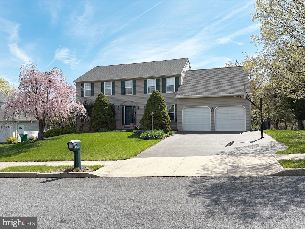 colonial home with a front yard, driveway, an attached garage, and roof with shingles