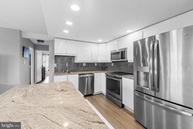 kitchen featuring light wood-style floors, white cabinets, stainless steel appliances, and tasteful backsplash