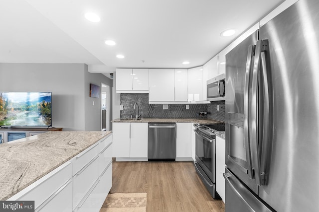 kitchen with modern cabinets, light stone countertops, light wood-style floors, stainless steel appliances, and white cabinetry
