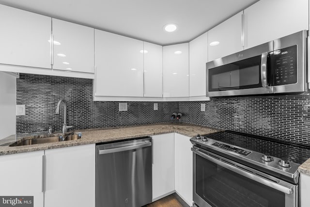 kitchen with a sink, backsplash, white cabinets, and stainless steel appliances