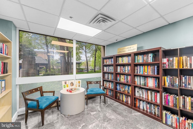 living area with visible vents, a paneled ceiling, and bookshelves