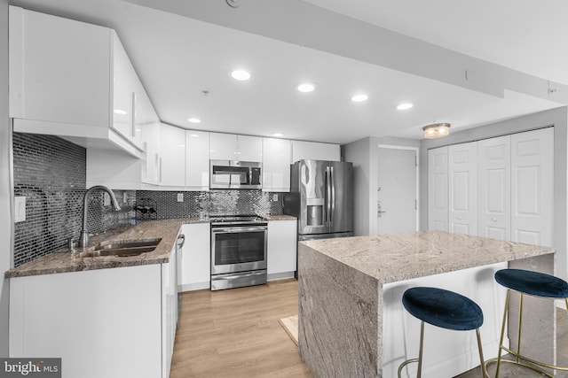 kitchen with a sink, light wood-style floors, a breakfast bar area, stainless steel appliances, and white cabinetry