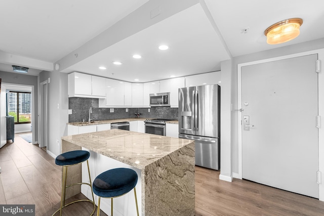 kitchen with white cabinets, backsplash, appliances with stainless steel finishes, and light wood-style flooring