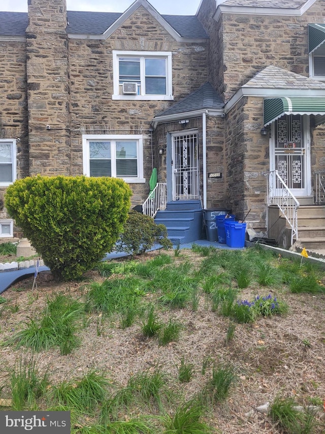 doorway to property featuring cooling unit, stone siding, a shingled roof, and a chimney
