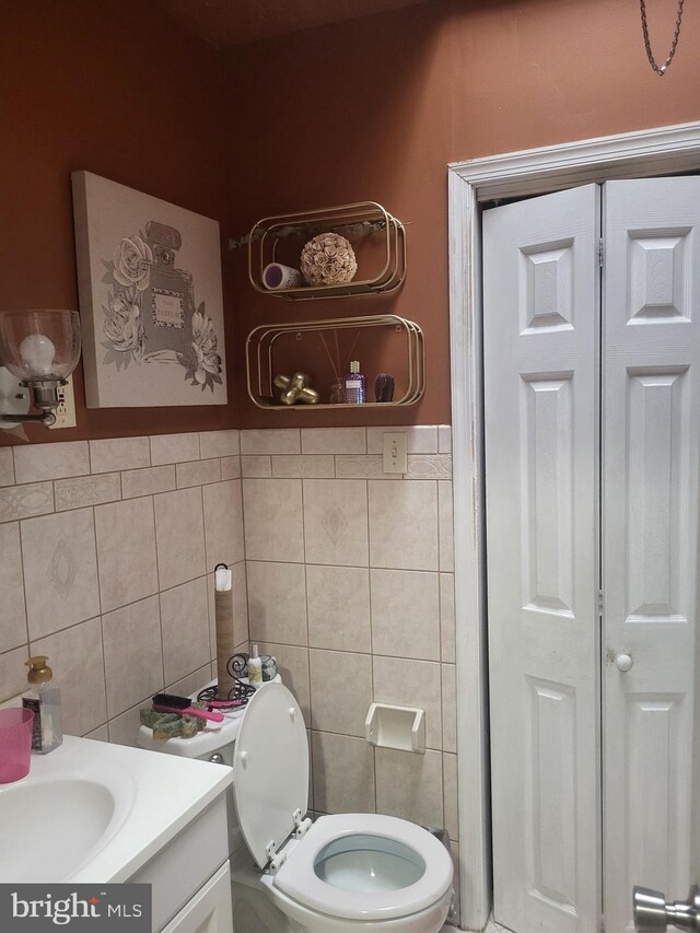 half bathroom featuring toilet, a closet, vanity, and tile walls