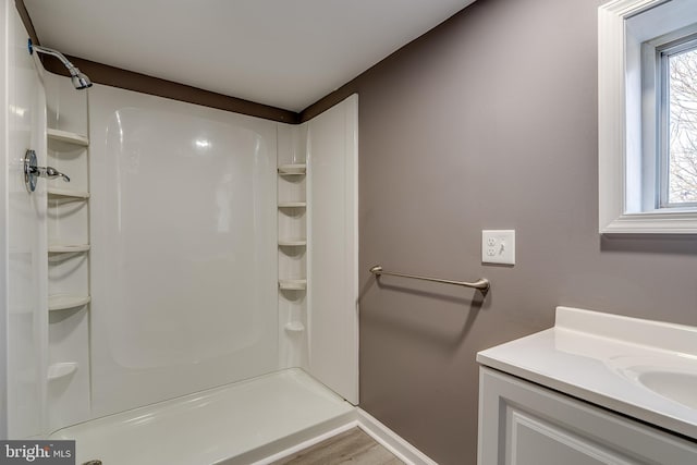 bathroom with baseboards, wood finished floors, vanity, and a shower