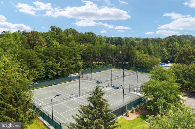 view of tennis court with fence and a wooded view