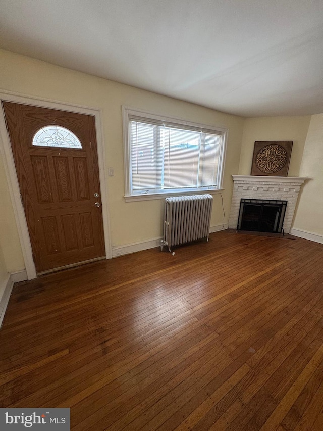 entryway with radiator heating unit, baseboards, a brick fireplace, and hardwood / wood-style floors
