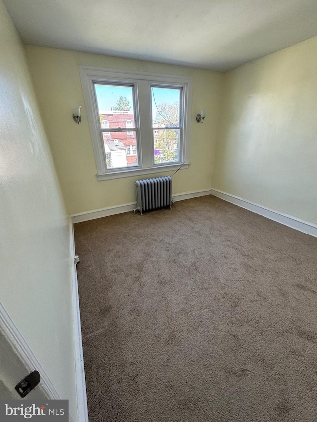 empty room featuring carpet floors, baseboards, and radiator heating unit