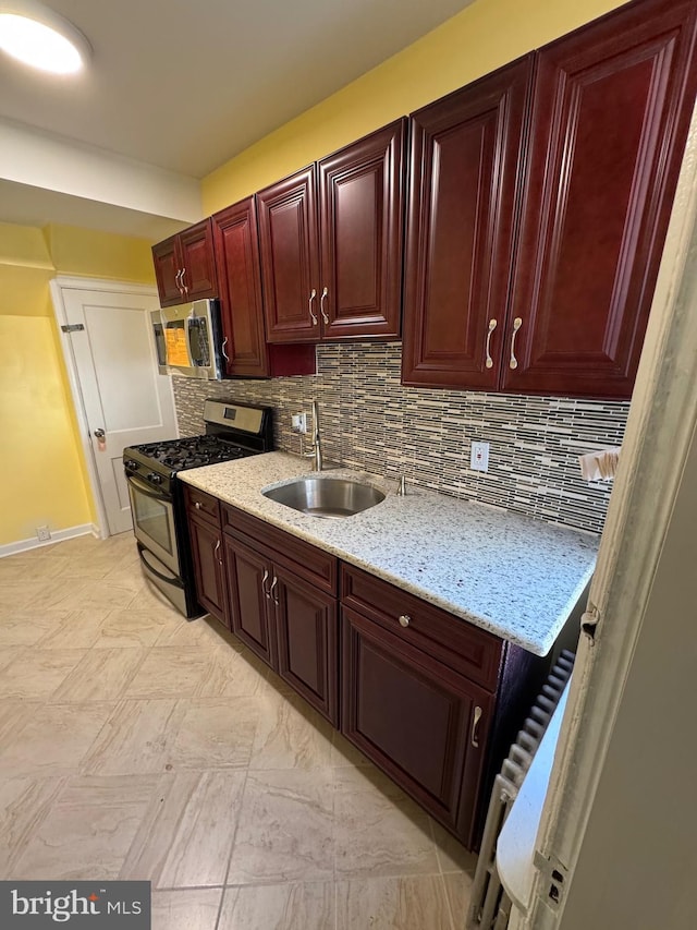 kitchen featuring dark brown cabinets, light stone countertops, appliances with stainless steel finishes, a sink, and tasteful backsplash
