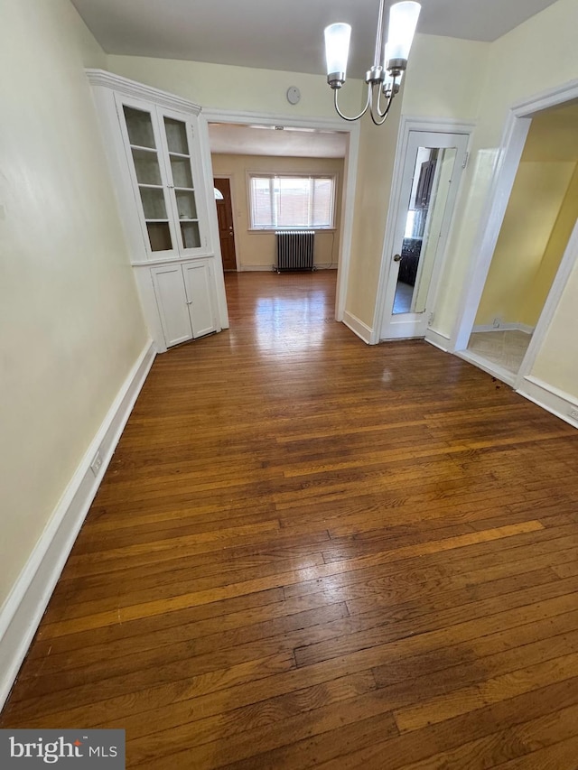 unfurnished dining area with an inviting chandelier, radiator, dark wood-type flooring, and baseboards