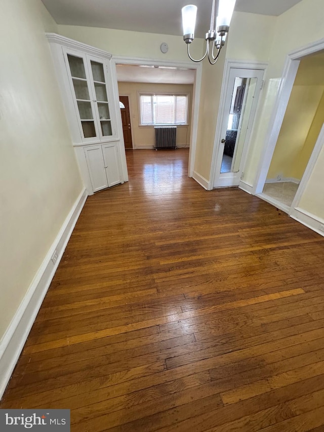 unfurnished dining area with baseboards, dark wood-style flooring, radiator heating unit, and a chandelier