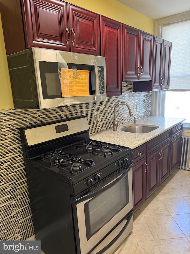 kitchen featuring backsplash, a sink, light stone counters, reddish brown cabinets, and stainless steel appliances