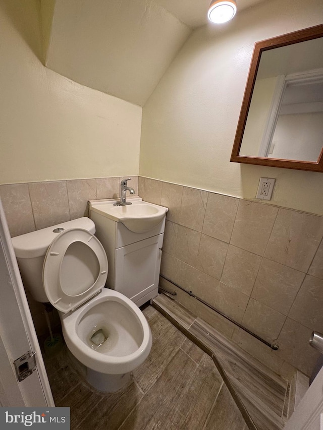 bathroom featuring vanity, lofted ceiling, toilet, and tile walls
