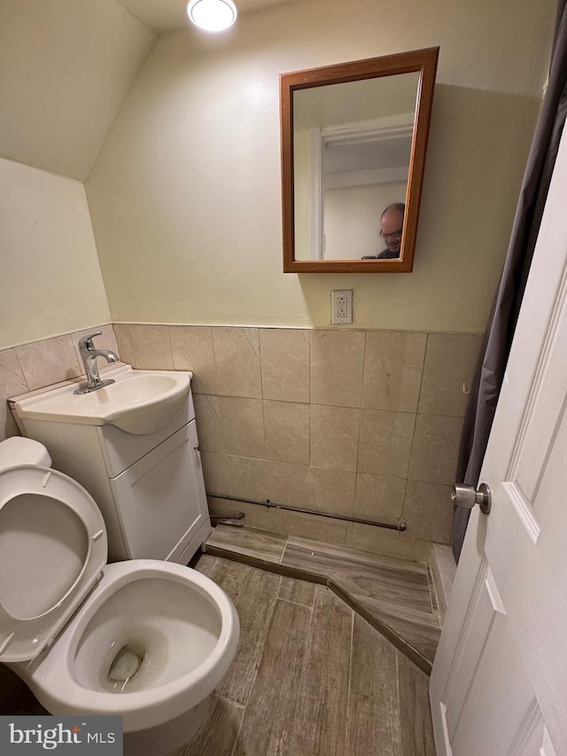 bathroom with vanity, toilet, a wainscoted wall, tile walls, and vaulted ceiling