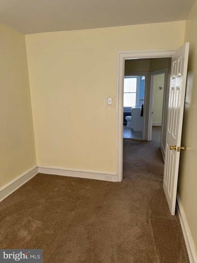 unfurnished room featuring baseboards and dark colored carpet