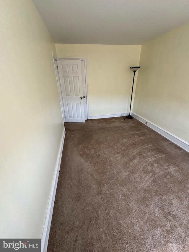 unfurnished room featuring baseboards and dark carpet