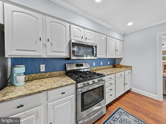 kitchen featuring white cabinetry, appliances with stainless steel finishes, light stone countertops, ornamental molding, and wood finished floors